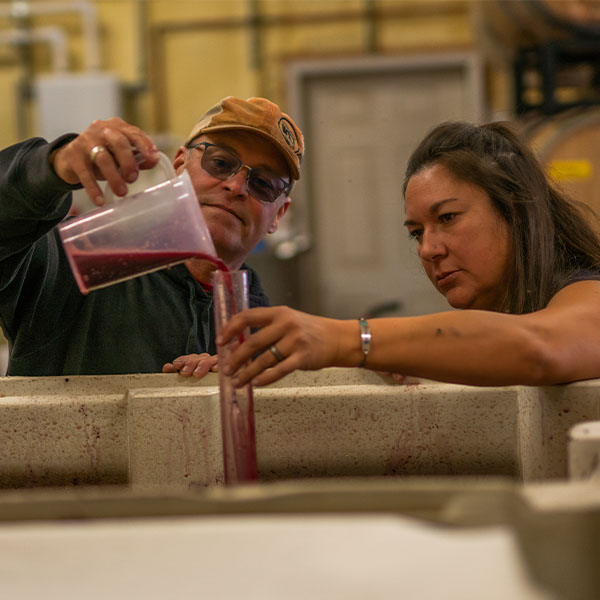 Two people pour red liquid into containers.