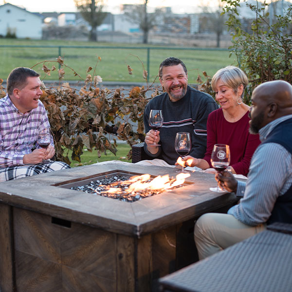Friends enjoying wine by outdoor fire pit.