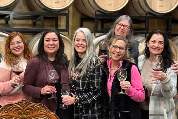 Group of smiling women holding wine glasses in cellar.