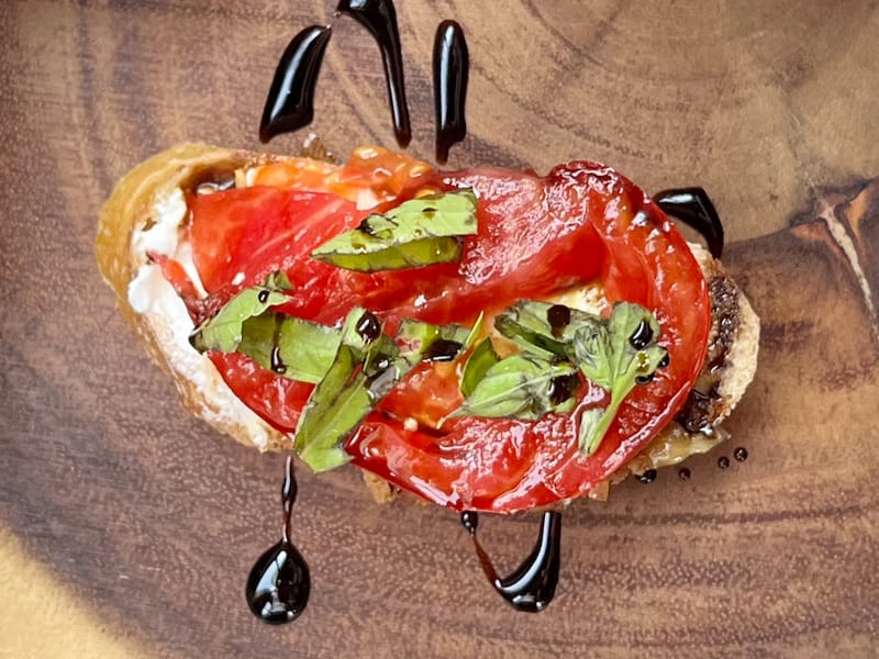 Tomato bruschetta with balsamic drizzle on wooden plate.