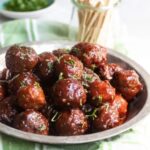 Plate of glazed meatballs garnished with herbs.