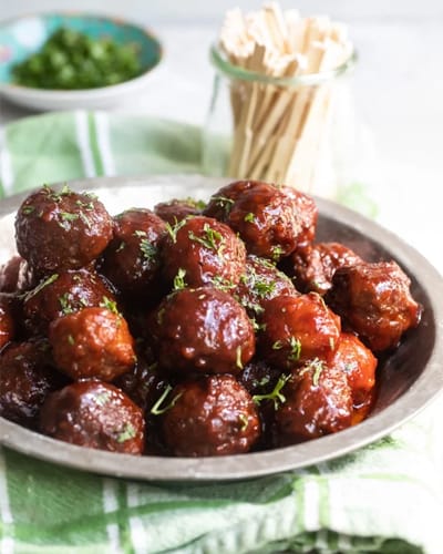 Plate of glazed meatballs garnished with herbs.