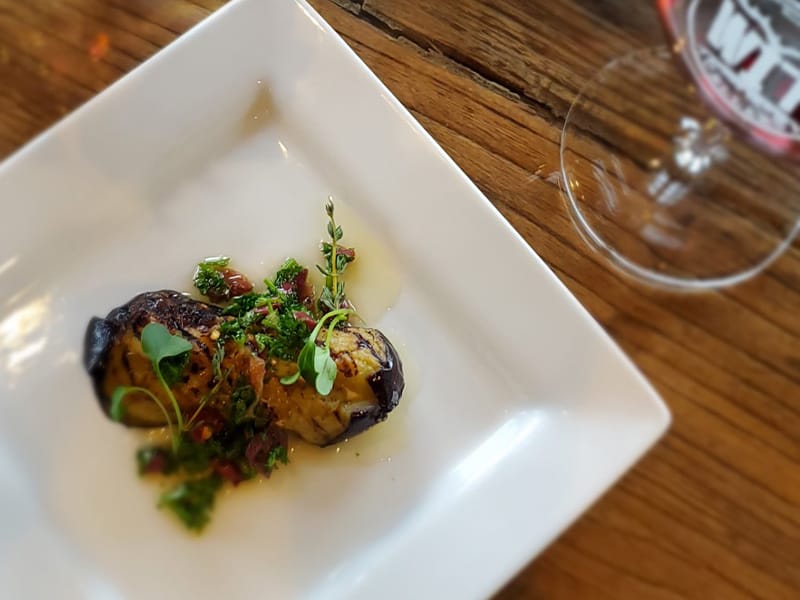 Grilled eggplant dish with herbs on white plate.