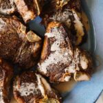 Grilled lamb chops with sauce on blue plate.