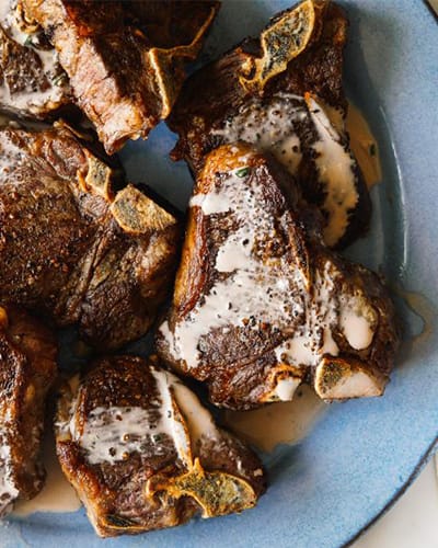 Grilled lamb chops with sauce on blue plate.