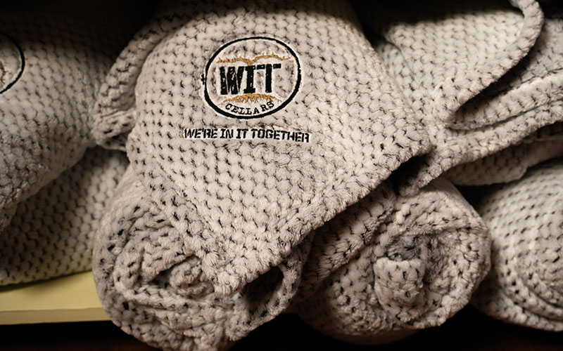 WIT Merch_0008_WIT_Product Lifestyle Shoot_11.23.2021-02643 Cozy gray WIT Cellars branded blanket stack.