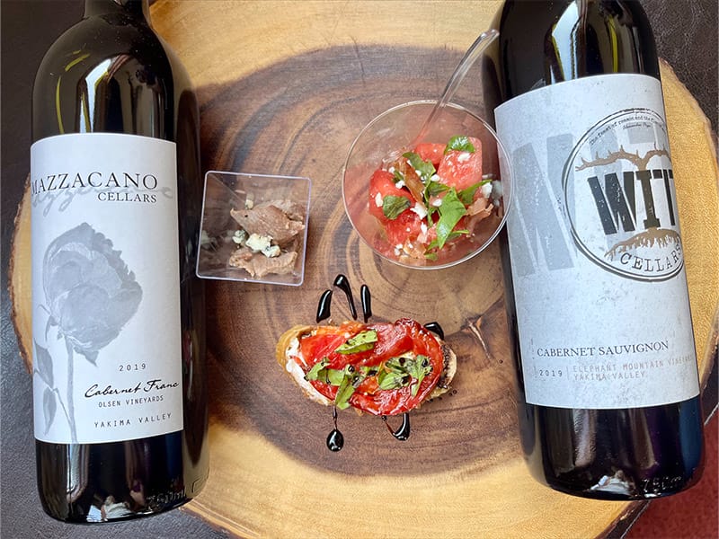 Two wine bottles with appetizers on wooden board.