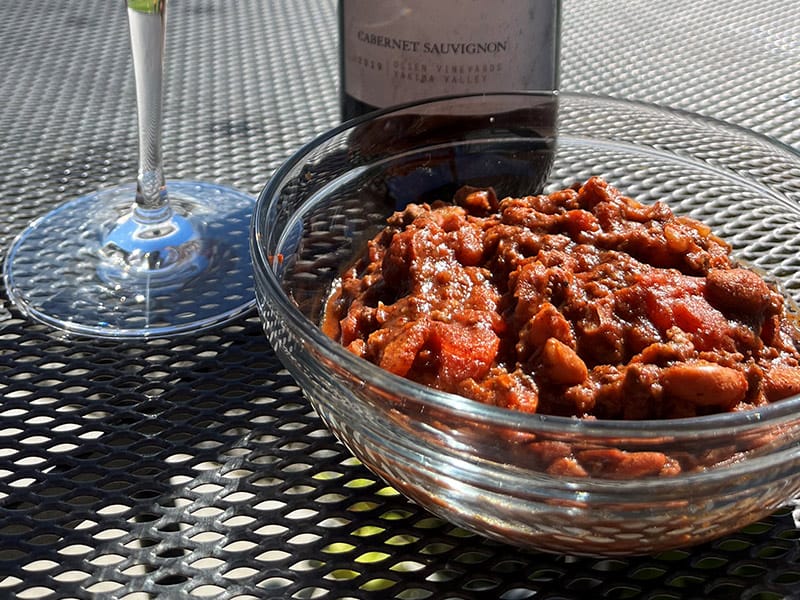 Bowl of chili with wine glass outdoors.