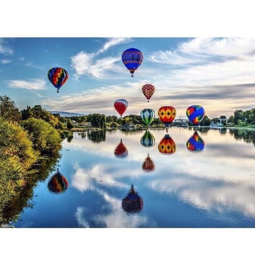 Balloon-Rally-2024 Colorful hot air balloons reflect on a serene lake.