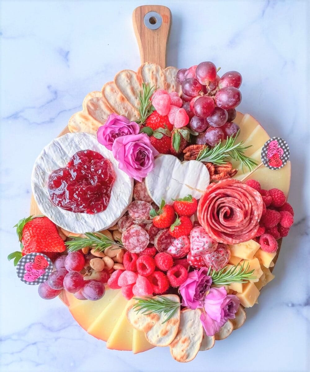 Colorful charcuterie board with cheese, fruit, and flowers.