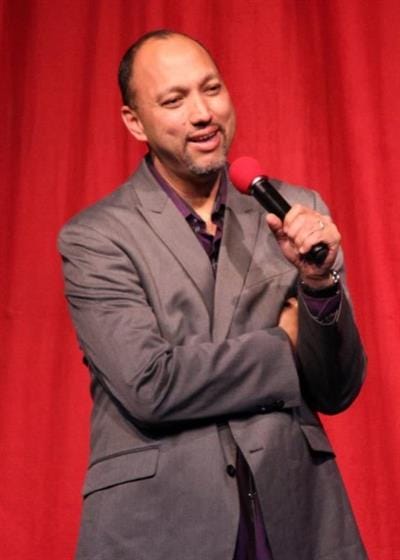 Kermet-Apio Man in suit speaking on stage with microphone.