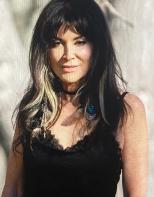 Woman with dark hair and lace top outdoors.