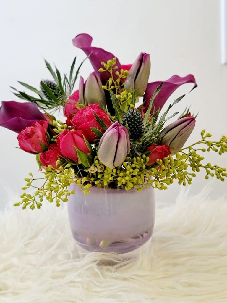Vday-glassybaby-centerpiece Vibrant flower arrangement in pink and purple vase.