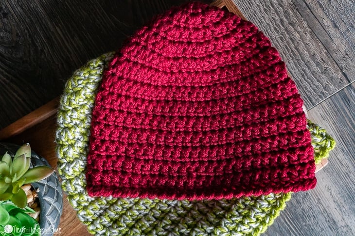 Red and green crochet hats on wooden surface.