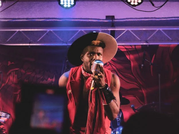 Singer performs on stage with hat and microphone.