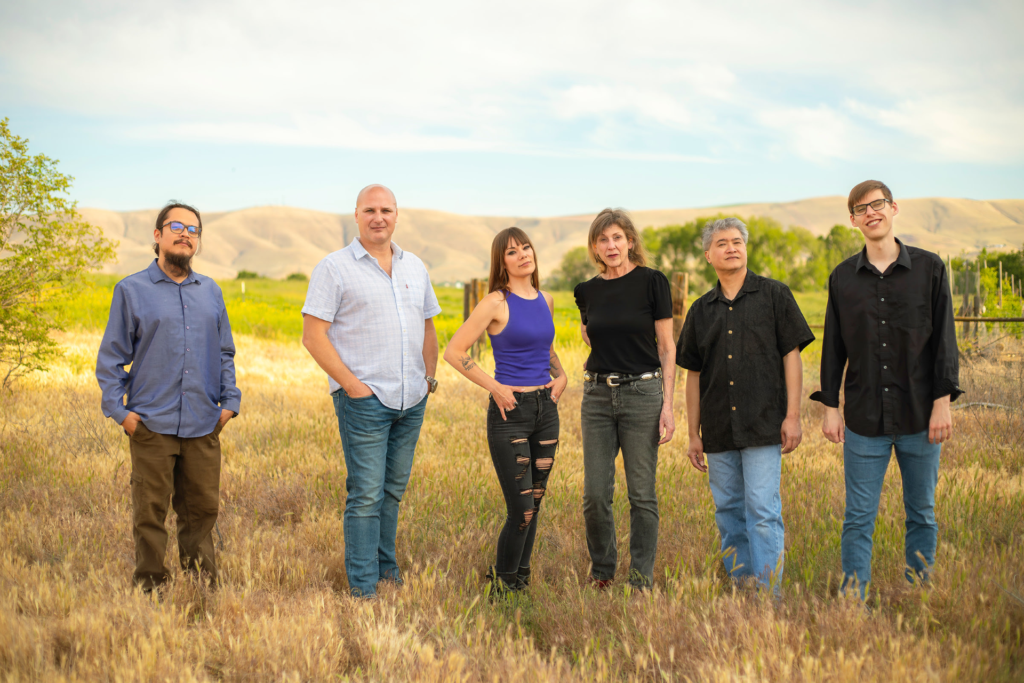 Six adults standing in grassy field with hills
