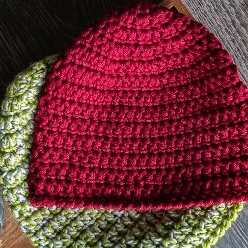 Red and green crochet hats on wooden surface.