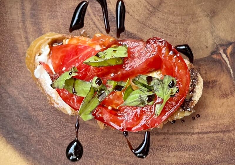 Tomato bruschetta with balsamic drizzle on wooden plate.
