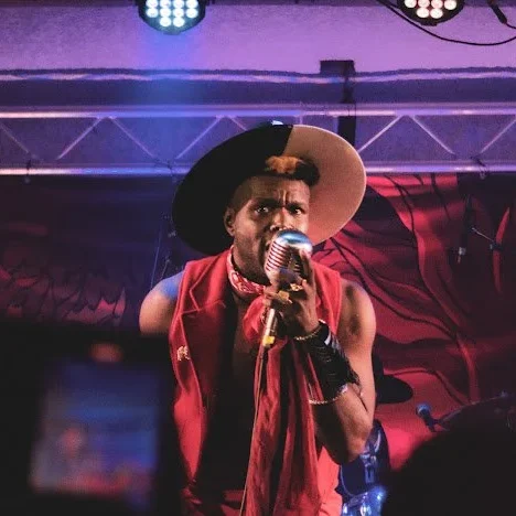 Singer performs on stage with hat and microphone.