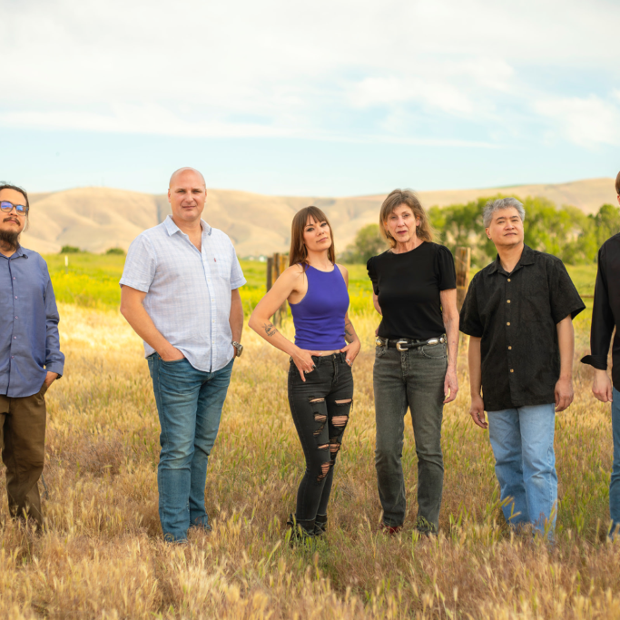 Six adults standing in grassy field with hills