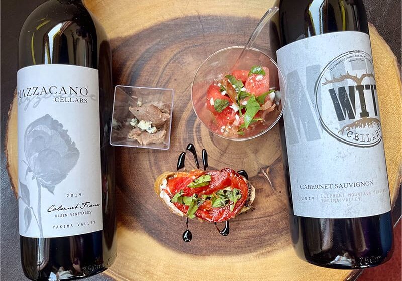 Two wine bottles with appetizers on wooden board.