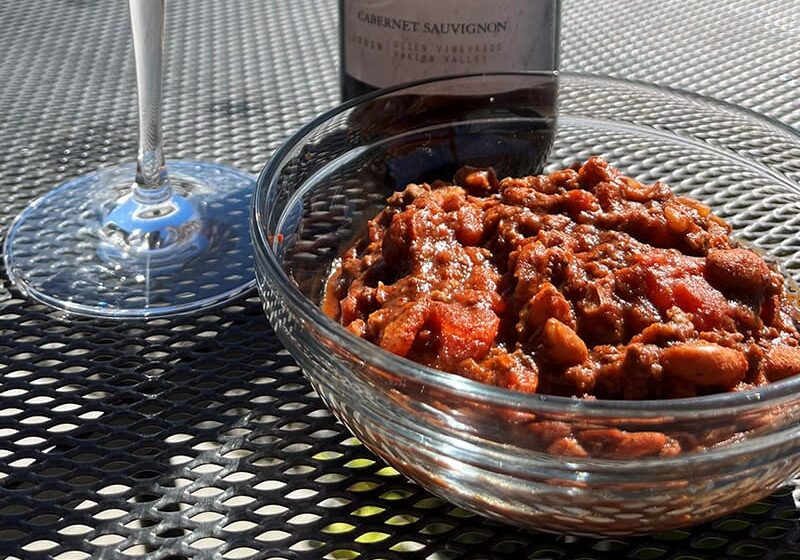 Bowl of chili with wine glass outdoors.